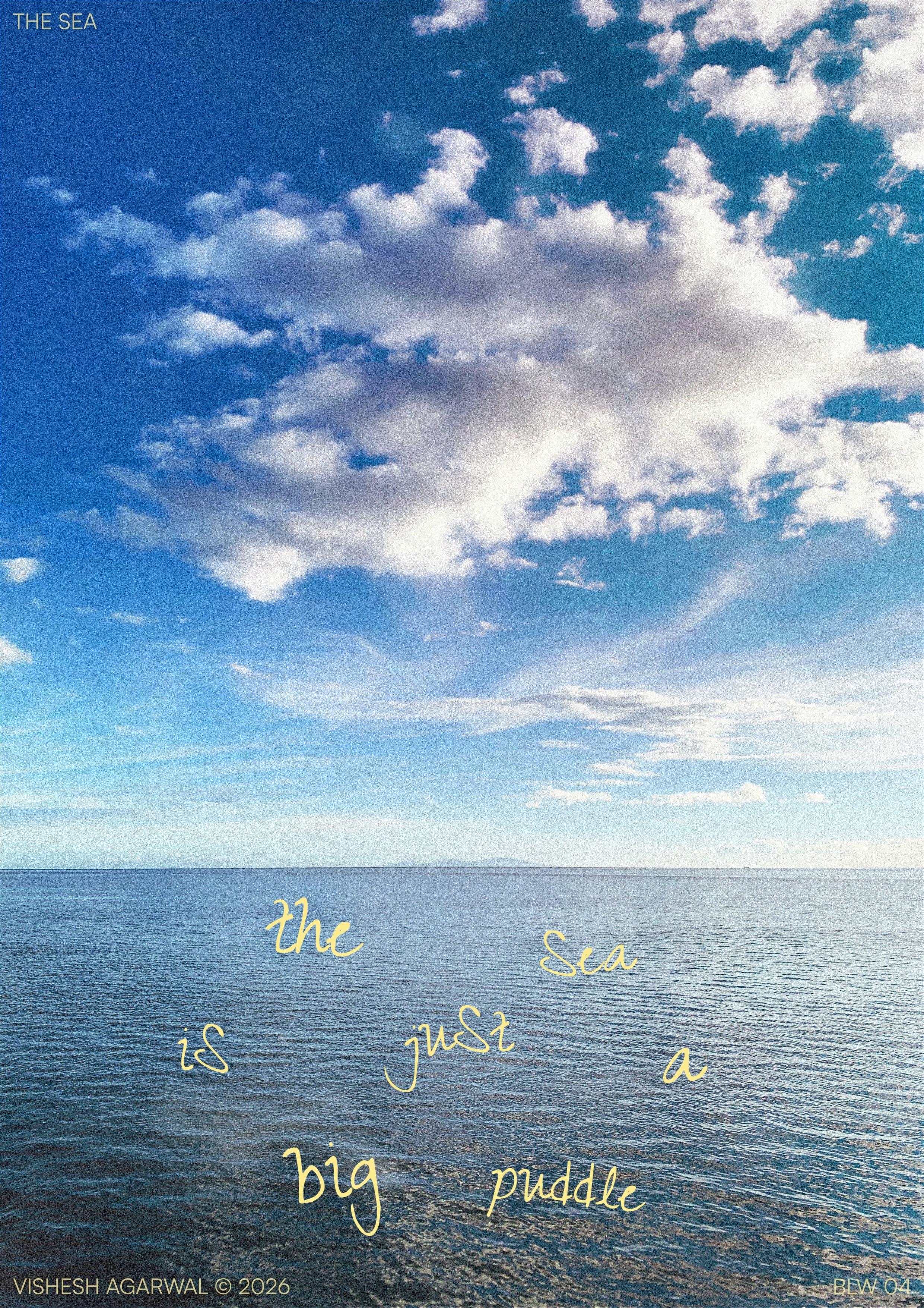A grainy photograph of a vast blue sea beneath a bright sky filled with soft, sprawling clouds. Yellow handwritten words across the water read, “The sea is just a big puddle,” playfully shrinking an immense landscape to a familiar childhood discovery and reminding us how wonder can make even the largest things feel simple.